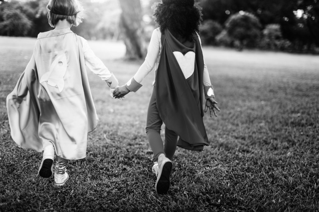 Children wearing capes, holding hands and running together